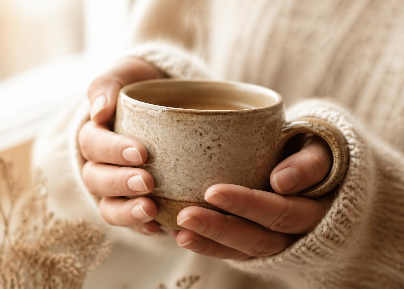 Two hands cradling a warm handmade ceramic coffee mug