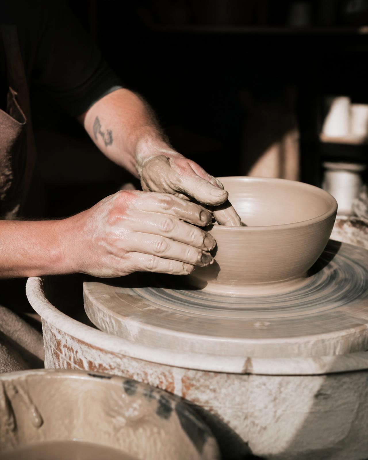 Potter's hands shaping wet clay on a spinning pottery wheel in a sunlit studio