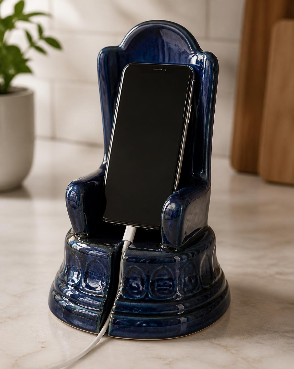 Handmade ceramic cell phone stand holding a phone upright on a wooden desk